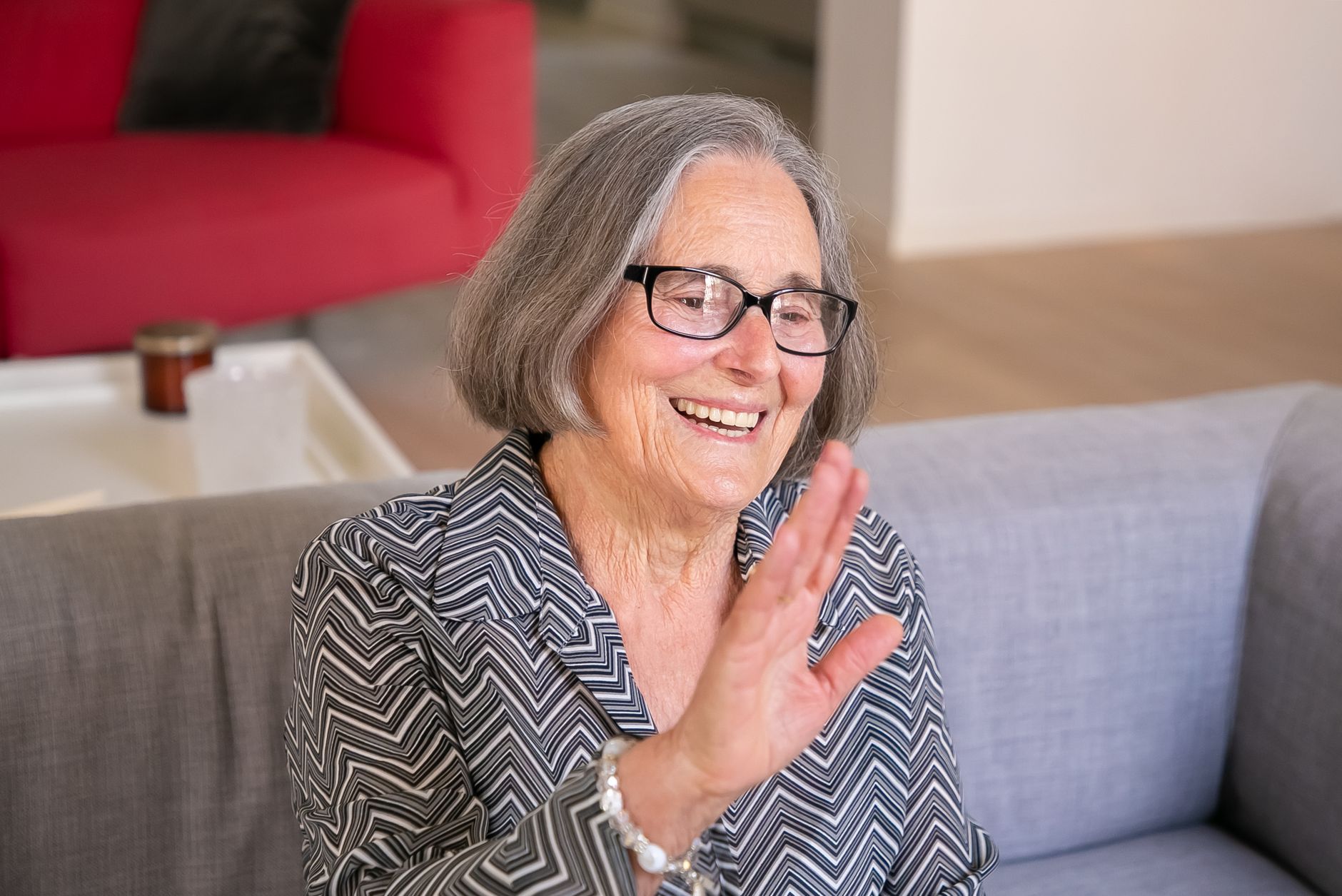 Smiling senior woman with glasses sitting comfortably on a couch at home